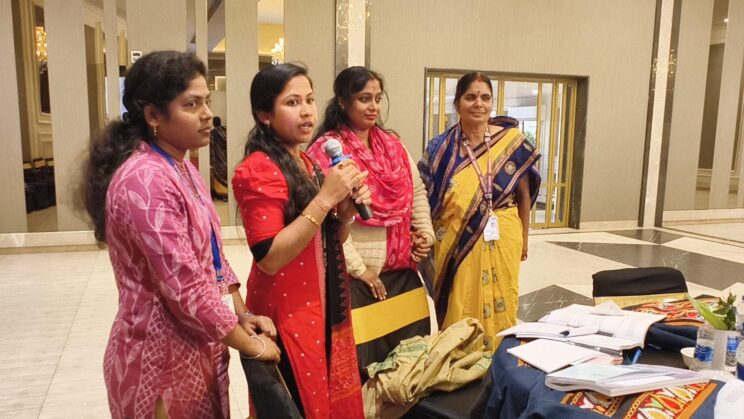 Close up of a group of 4 female teachers standing at their table, one of them speaking into a mic. 