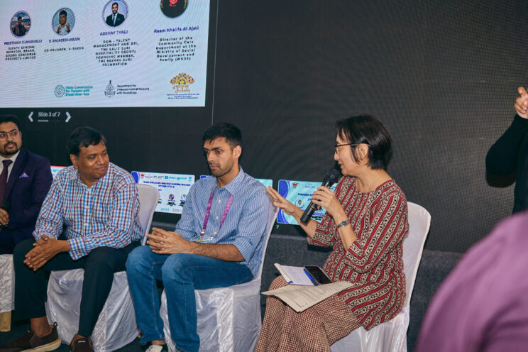 Mikiko speakng with a microphone in her hand, while the panellists listen to her.