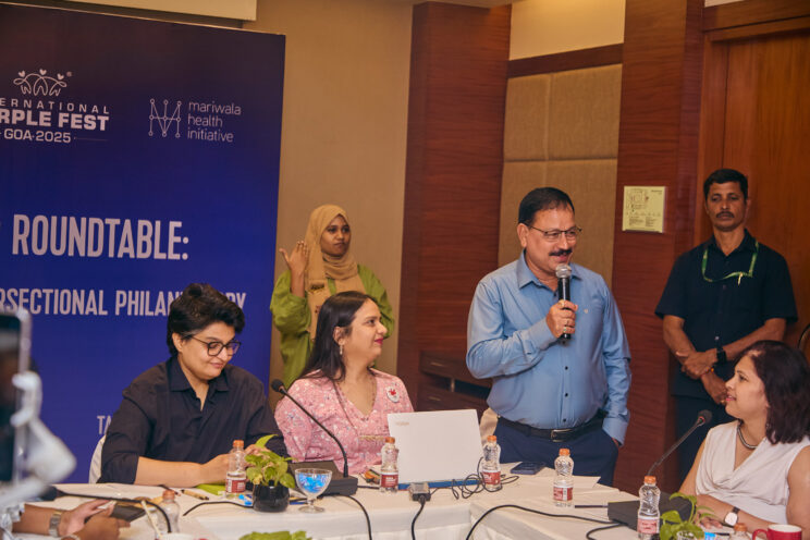 Shri Subhash Phal Dsesai standing next to Nidhi Goyal and Raj Mariwala on the left. He is speaking into a microphone. There is an ISL interpreter behind him, and one of the participants, Swarnalatha J on the right. The funder roundtable banner is visible right at the back. 