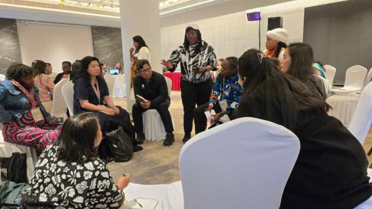 One of the groups sitting on chairs in a circle with one person on the floor with chart paper. Loretta Ruby is standing and speaking to the group.