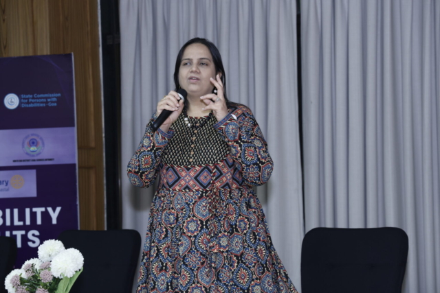 Nidhi Goyal standing on a small stage, speaking into a mic.