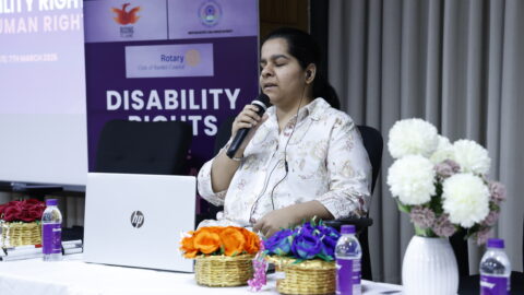 Anchal Bhatheja sitting on a chair, with a laptop in front of her, speaking into a mic