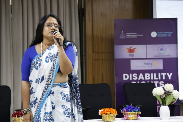 Sanchita Ain standing on a stage, speaking into a mic
