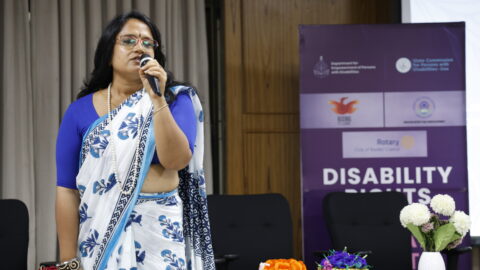 Sanchita Ain standing on a stage, speaking into a mic