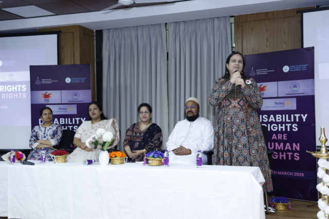 Panel of speakers on a stage. Nidhi Goyal is standing and speaking into a mic. On her right are other speakers.