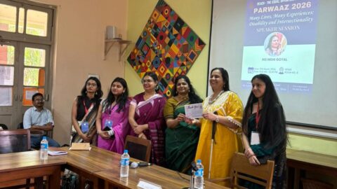 A group photo with Nidhi Goyal and the organisers. She is holding a certificate and smiling at the camera. Behind them is a projector with the details of the event on it - "Parwaaz 2026, Many Lives, Many Experiences: Disability and Intersectionality, Speaker Session: Nidhi Goyal" with the date, time, and venue at the bottom.