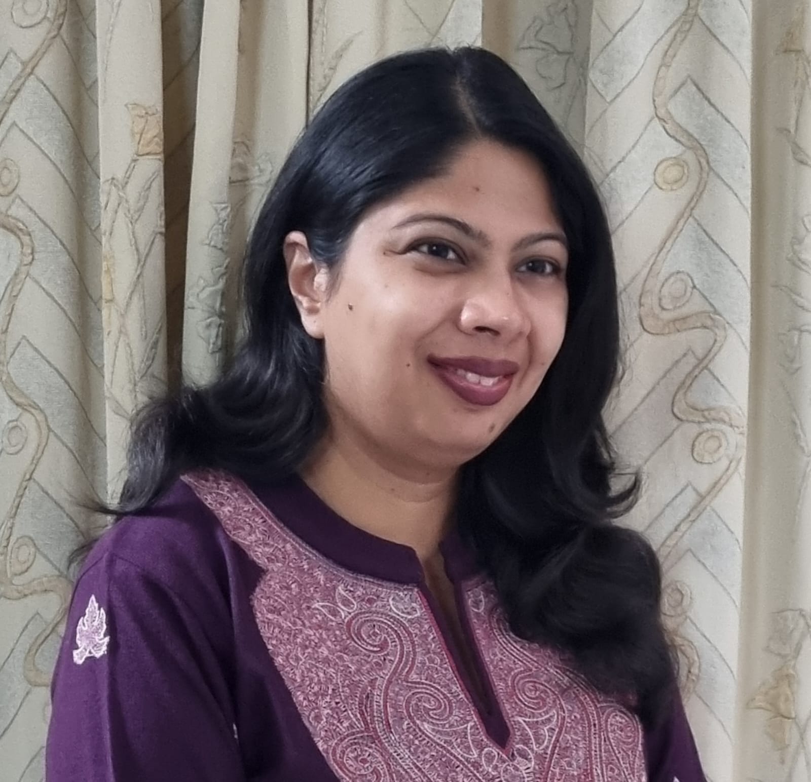 Akankshi Srivastava is an Indian woman with long wavy dark hair, one side tucked behind her ear. She is wearing a dark purple kurta with light purple designs in the front.