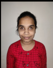 Dhanashri Gawande is an Indian woman standing in front of a white wall. Her hair is dark and tied up at the back. She is wearing a red kurti.