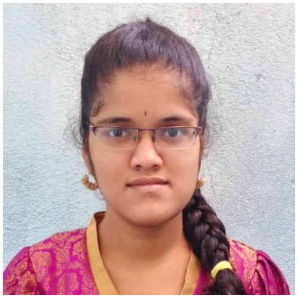 Divya S is an Indian woman with dark black hair tied in a braid over her shoulder. She is wearing glasses, and a pink kurta with golden borders at the collar.