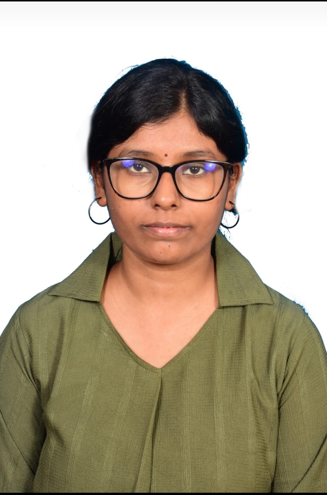 Malavika B is an Indian woman, sitting in a studio with a white background. She has dark hair that is tied back. She is wearing glasses, and a green collared top.