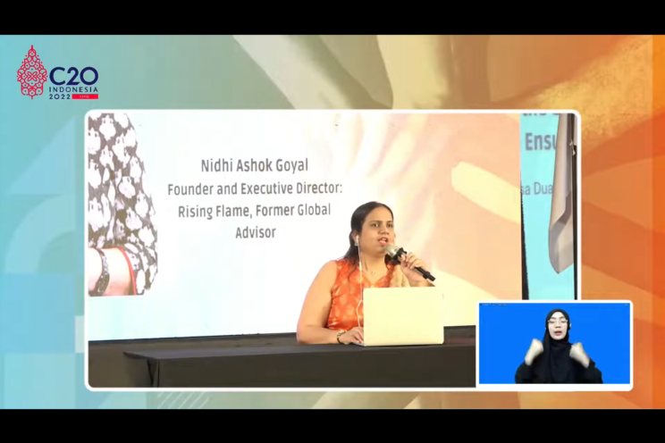 Screenshot from the Youtube livestream. Inside a C20 Indonesia 2022 branded frame is a video of Nidhi Goyal sitting at a long table with a mic in hand, speaking. Her laptop is in front of her. Behind her is a large projector on which is a photo of her and her name, designation: "Nidhi Ashok Goyal, Founder and Executive Director: Rising Flame, Former Global Advisor." On the bottom left side of the screen is a small window with a sign language interpreter signing.