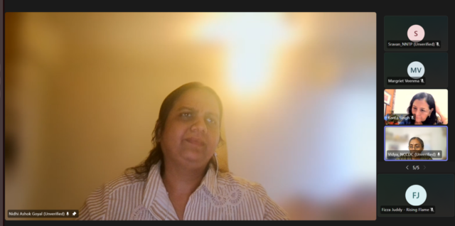 Screenshot from a Teams webinar. Nidhi Goyal is pinned on the screen with a few other participants' windows on the right side. Nidhi is wearing a white blue striped collar shirt with her some of her hair pulled back. She is speaking.