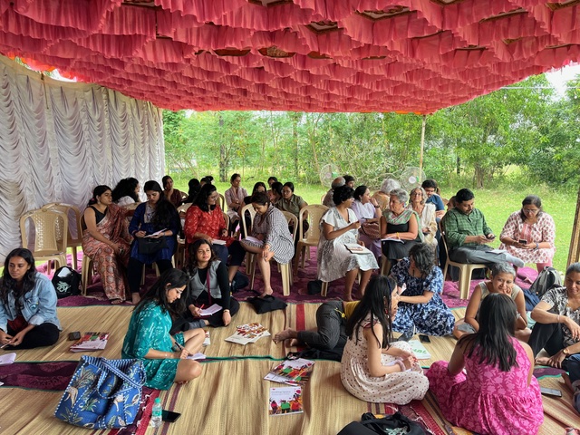 Discussions on Deconstructing Ableism, picture of all participants seated on chairs and the floor in a shaman style tent with the Rising Flame manuals. Green grass and trees in the background