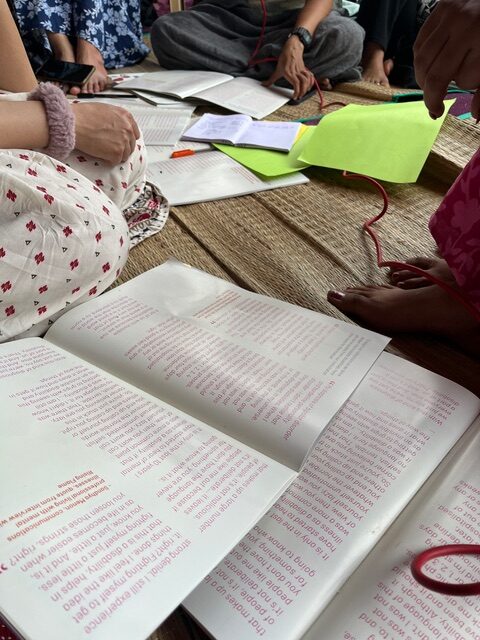 Picture with Rising Flame Manuals open, notebooks, colour papers and pens, seated participants hands and legs are seen during group work.
