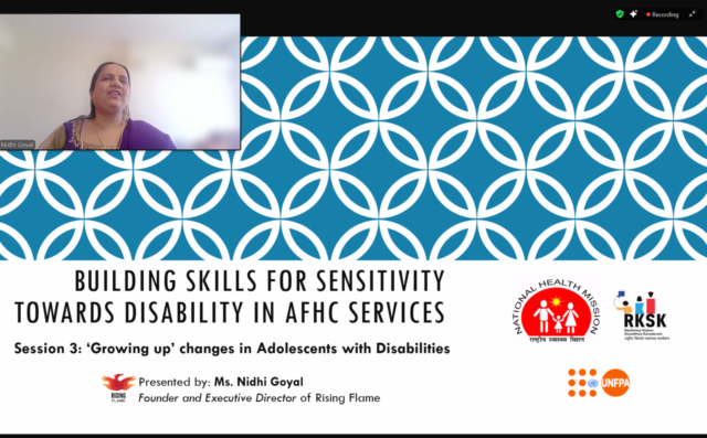 Screenshot of a Zoom webinar with a presentation displayed. A small window on the top left displays Nidhi Goyal on camera. Her background is blurred, she is wearing a purple suit with her hair pulled back. She is speaking. The presentation has the title of the session on it: "Building Skills for Sensitivity Towards Disability in AFHC Services. Session 3: Growing Up’ Changes in Adolescents with Disabilities. Presented by Ms. Nidhi Goyal. Founder and Executive Director of Rising Flame."