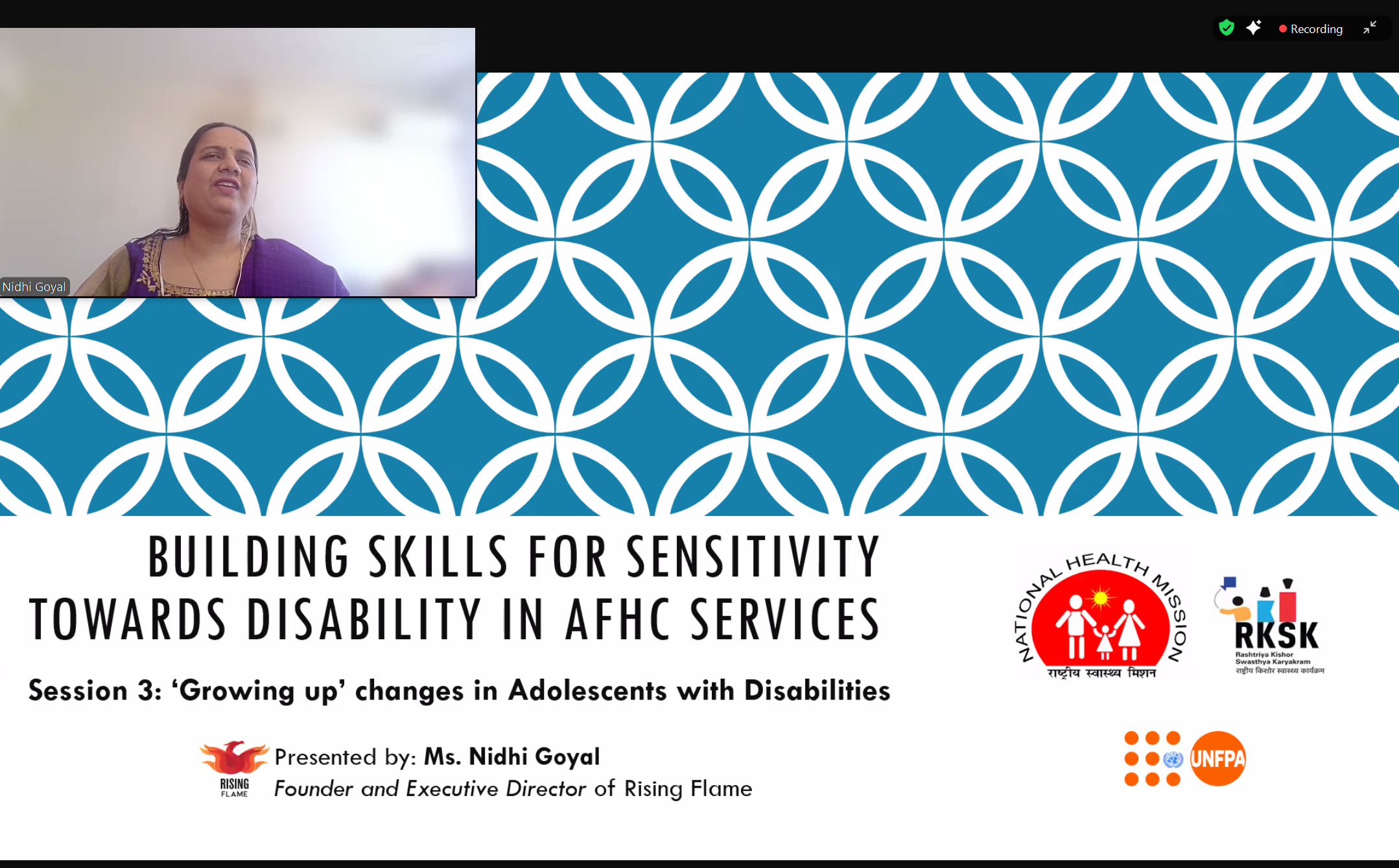 Screenshot of a Zoom webinar with a presentation displayed. A small window on the top left displays Nidhi Goyal on camera. Her background is blurred, she is wearing a purple suit with her hair pulled back. She is speaking. The presentation has the title of the session on it: "Building Skills for Sensitivity Towards Disability in AFHC Services. Session 3: Growing Up’ Changes in Adolescents with Disabilities. Presented by Ms. Nidhi Goyal. Founder and Executive Director of Rising Flame."